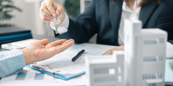Real estate agent handed over the key to new home, marking a successful investment in business of property, whether it be a house or an apartment. Real estate agent giving house key to customers.